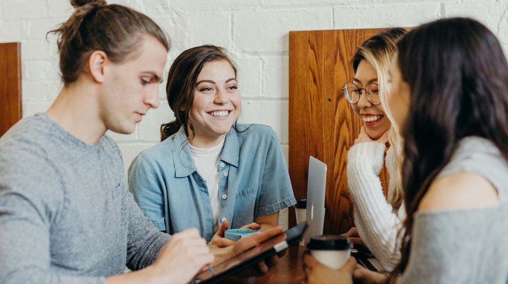 Four young people collaborating in a cafe with laptops