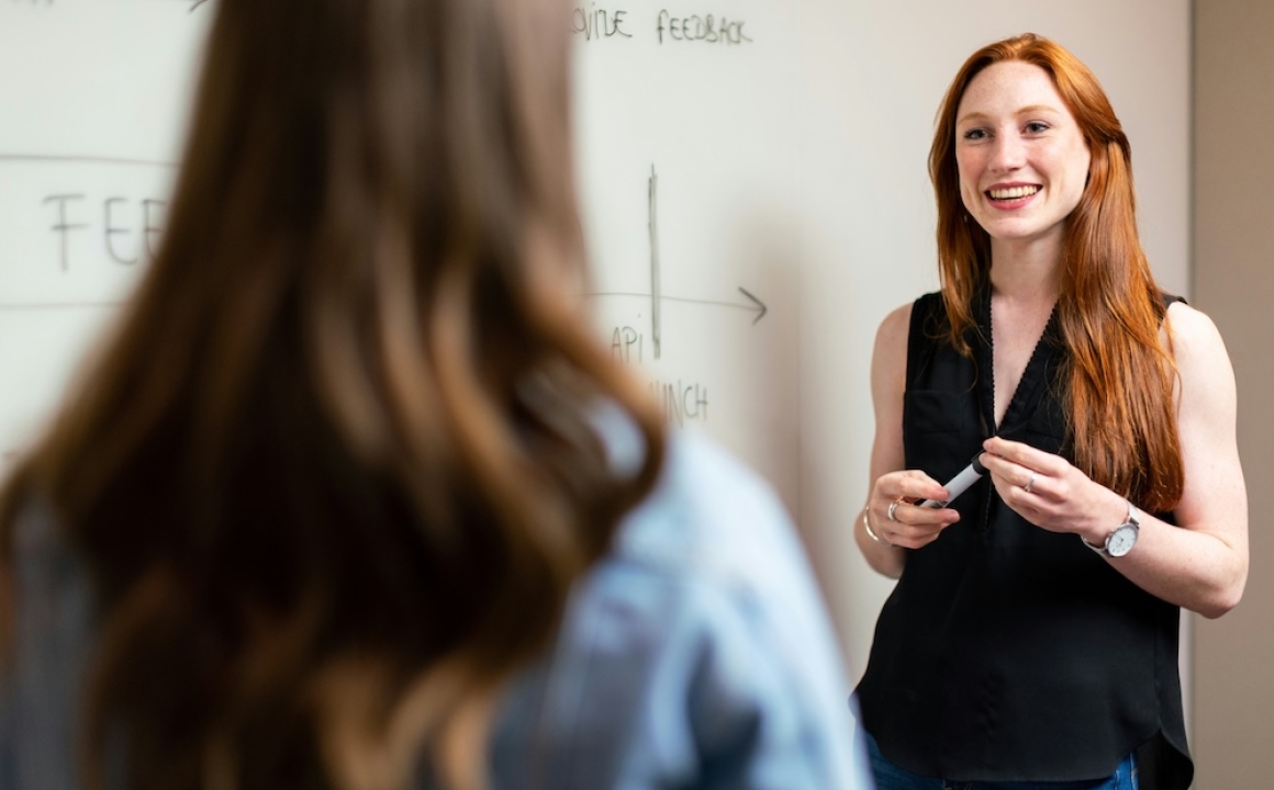 Female teacher standing in front of a whiteboard while talking with a student