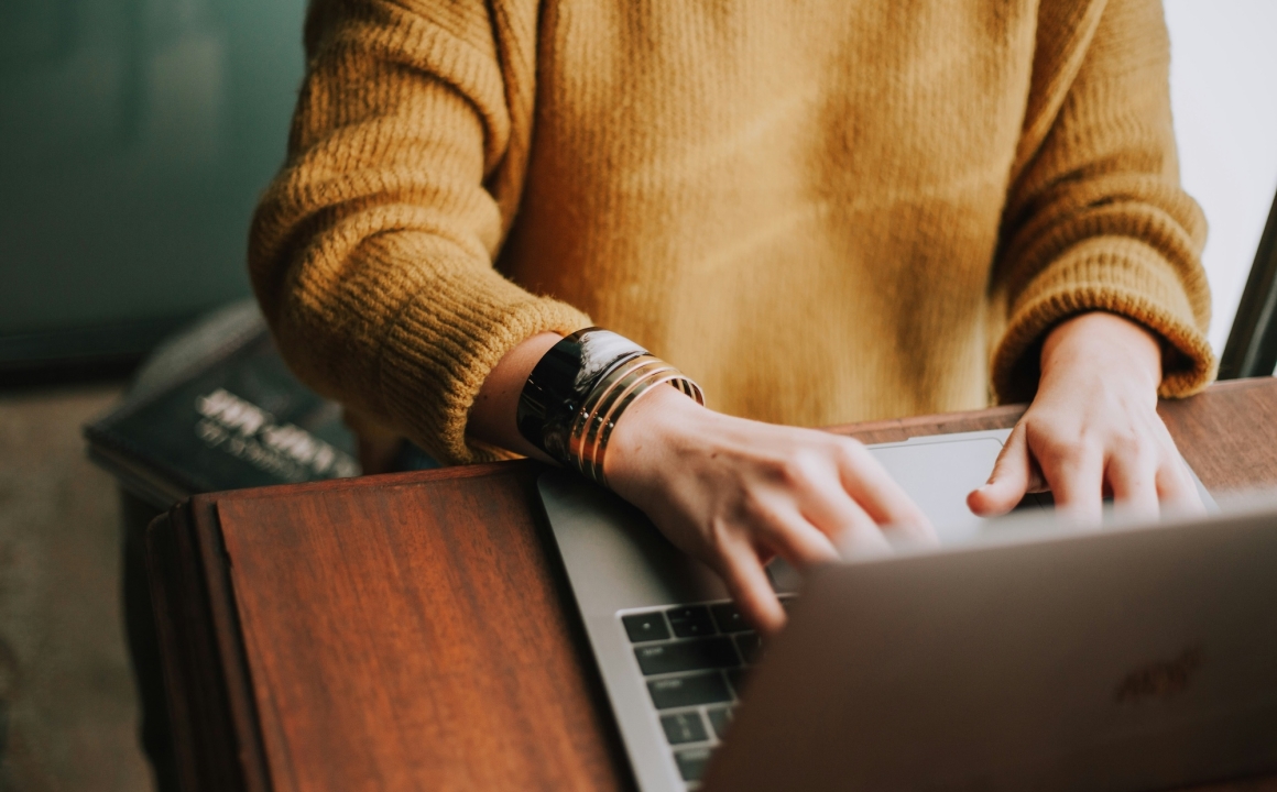 Person in orange sweater writing on a laptop