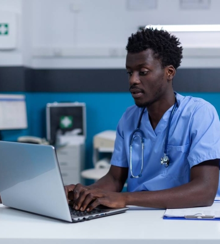 Nursing student in a clinic working on a laptop.