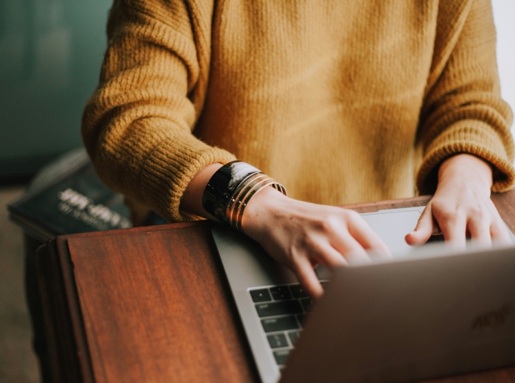 Person in orange sweater writing on a laptop